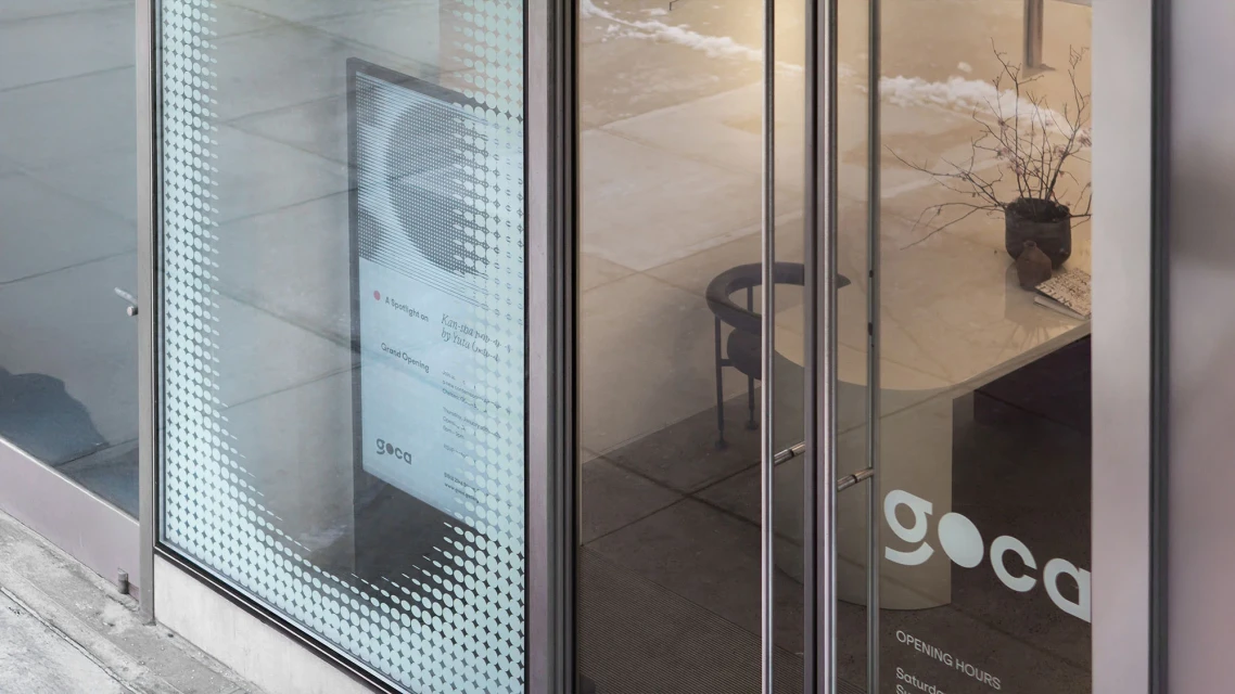 Exterior view of the Goca art gallery, featuring glass doors, a glimpse of the interior, and signage with opening hours.