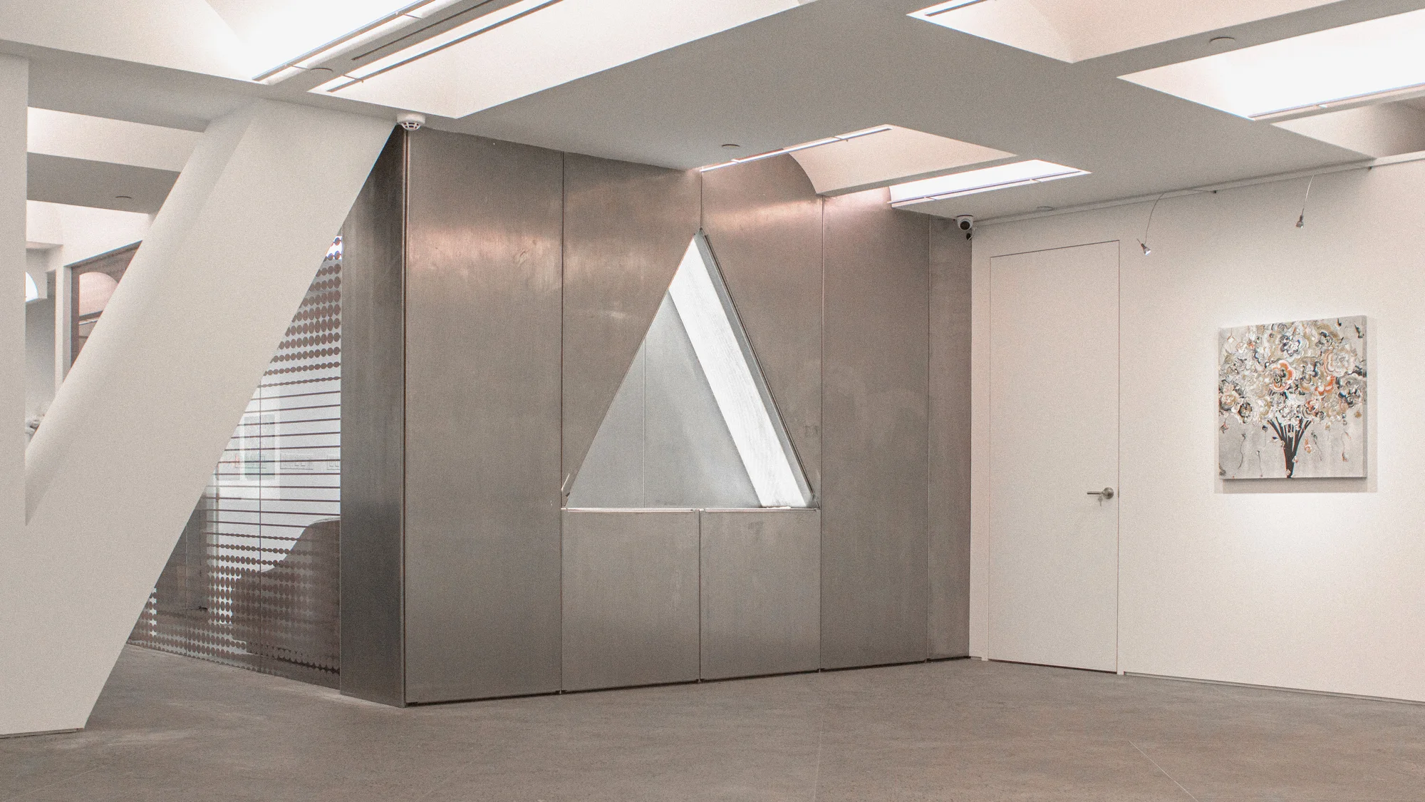 Modern art gallery interior with geometric architecture, concrete floor, white walls, interior door, and an abstract floral painting.