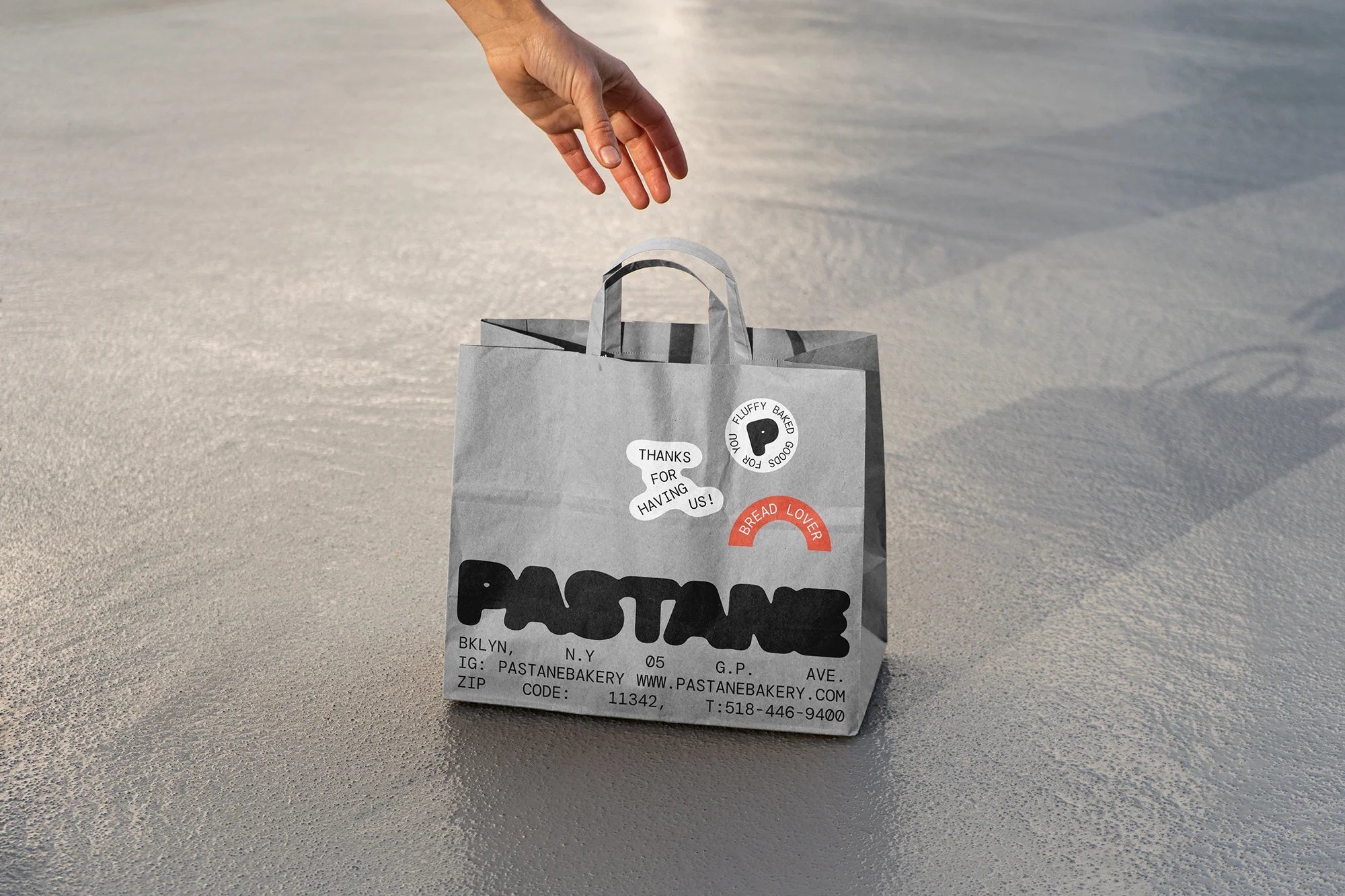 Paper bag from Pastane bakery in Brooklyn, New York, with the bakery's logo and contact details, plus some stickers on a neutral floor.
