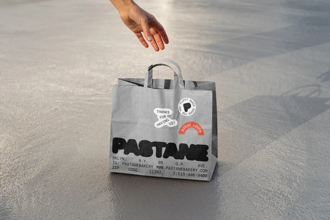 Paper bag from Pastane bakery in Brooklyn, New York, with the bakery's logo and contact details, plus some stickers on a neutral floor.