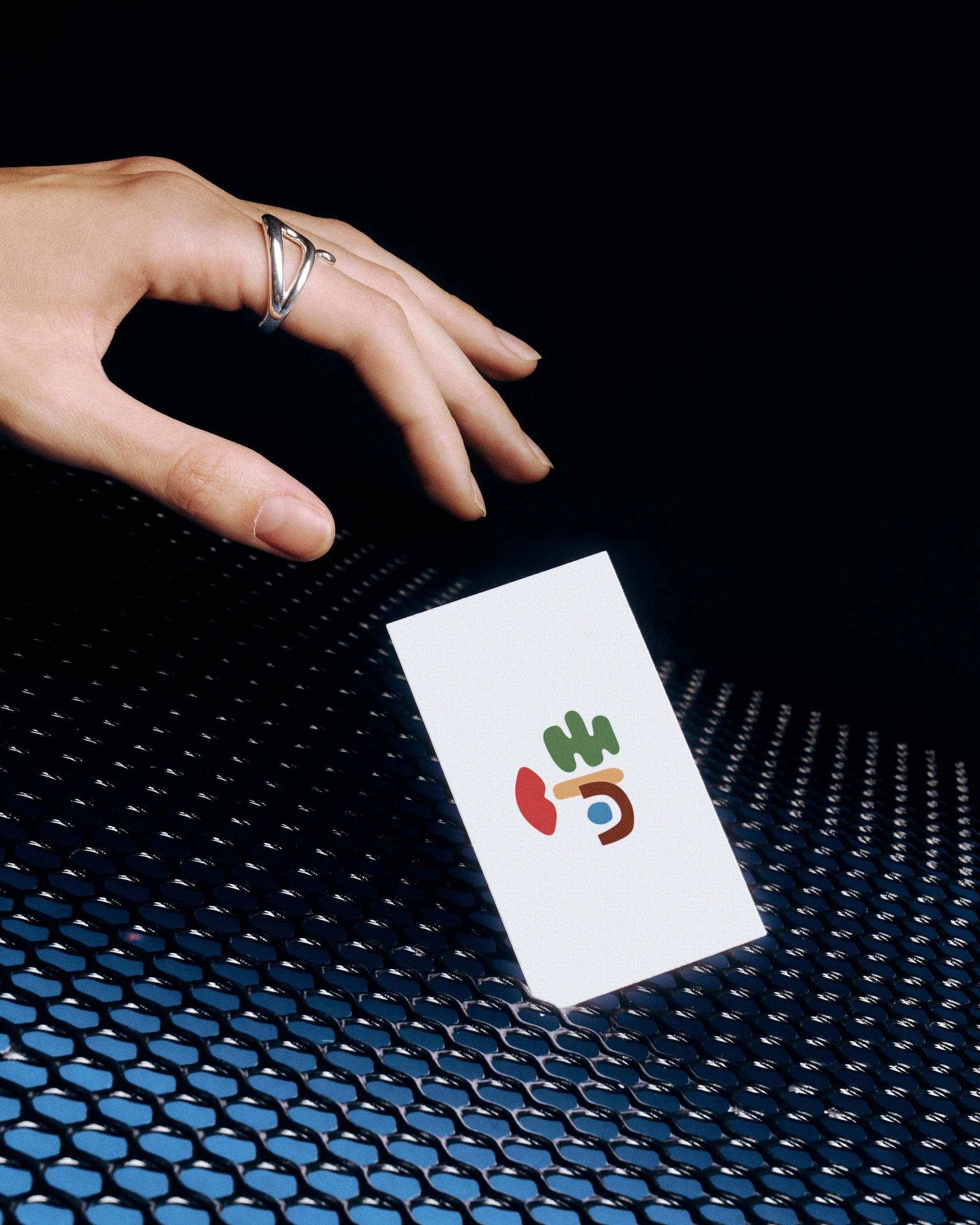 Hand reaches toward white business card with abstract illustration on a perforated metal surface with blue underlighting.