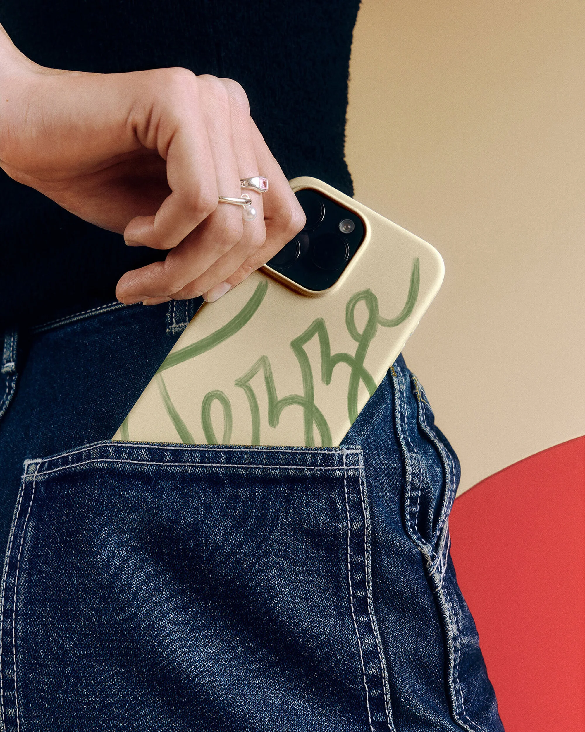 Close-up of a denim jean pocket containing a modern smartphone, showcasing a stylish case with a minimalist green design.