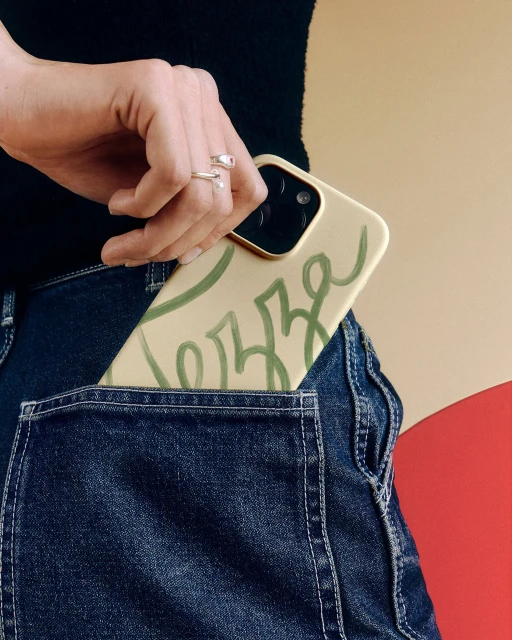 Close-up of a denim jean pocket containing a modern smartphone, showcasing a stylish case with a minimalist green design.