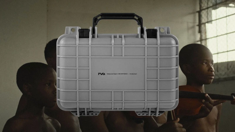 Grey hard case in the foreground with black handle, with blurred Black children in the background, one holding a violin.