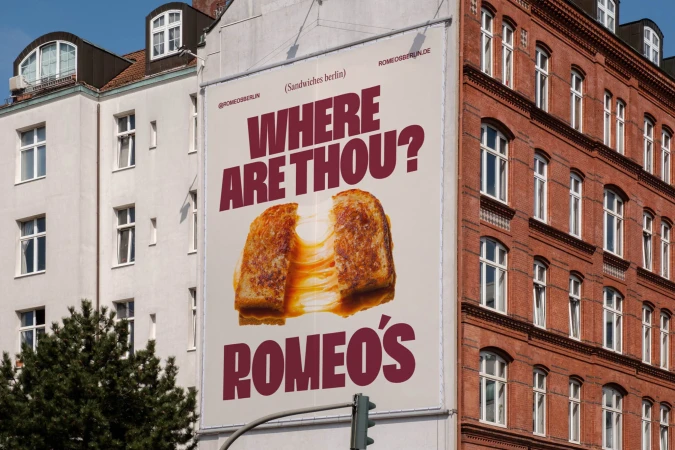 Advertising billboard featuring a grilled cheese sandwich on an urban building with text, promoting Romeo's in Berlin, Germany.