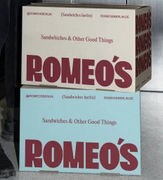 Two stacked branded boxes for Romeos with bold red typography against a textured concrete background.