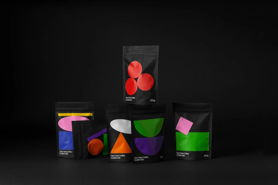Collection of Hey Hola Coffee Guatemala packages featuring colorful geometric designs against a dark background, minimalist aesthetic.