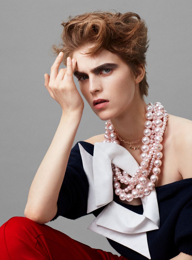 Fashion portrait of a model with fair skin, short brown hair, and a pearl necklace in a photo studio with a neutral grey background.