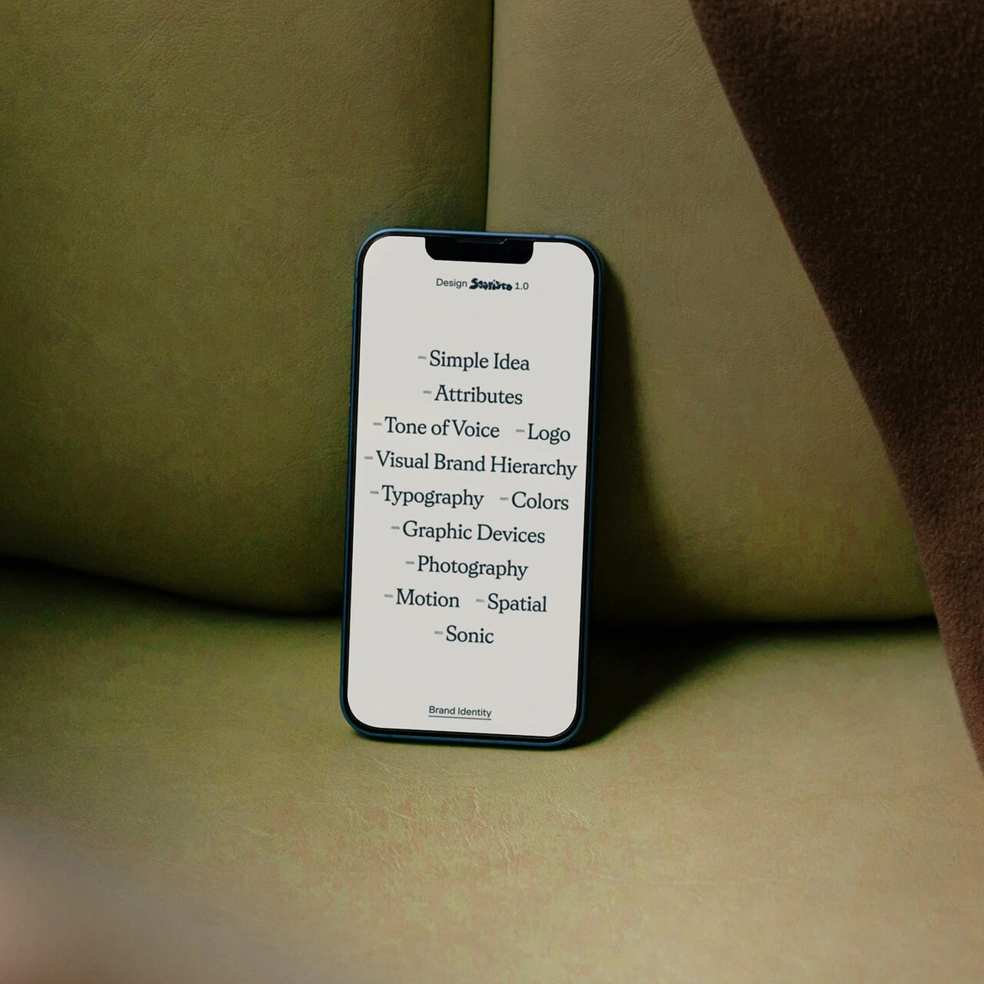 Mobile phone displaying design elements on a light green surface with a blurred beige fabric background. Branding and identity mockup.