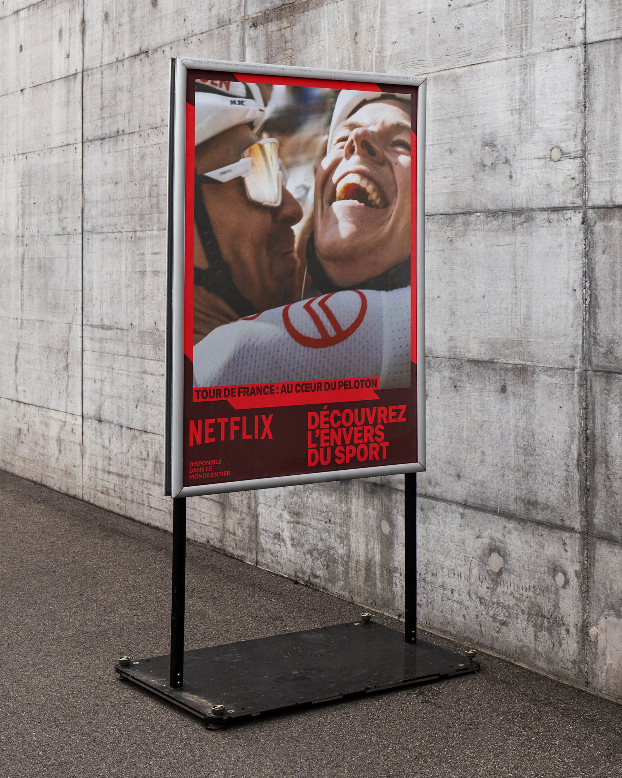Outdoor advertisement for Netflix's 'Tour de France: Au Coeur du Peloton' showing two cyclists embracing on the road.