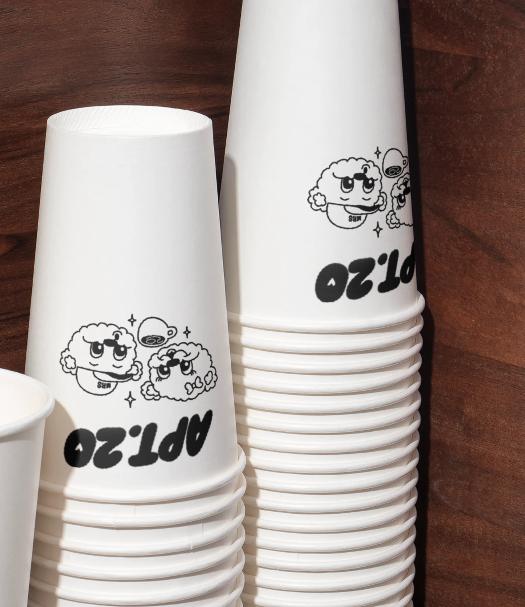 Stack of white paper cups with cartoon graphic and Apt. 20 logo against wood background for coffee or beverage service.