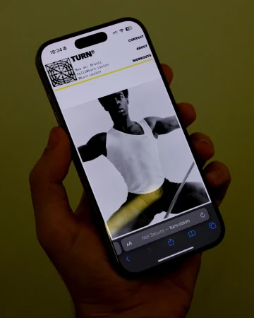 Hand holding a smartphone displaying a mobile website with a black and white dancer photo for TURN brand identity.