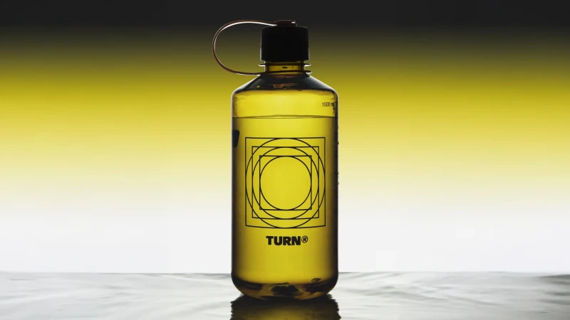 Water bottle filled with yellow liquid. Clear plastic with black lid, geometric logo design. Studio shot with light background.