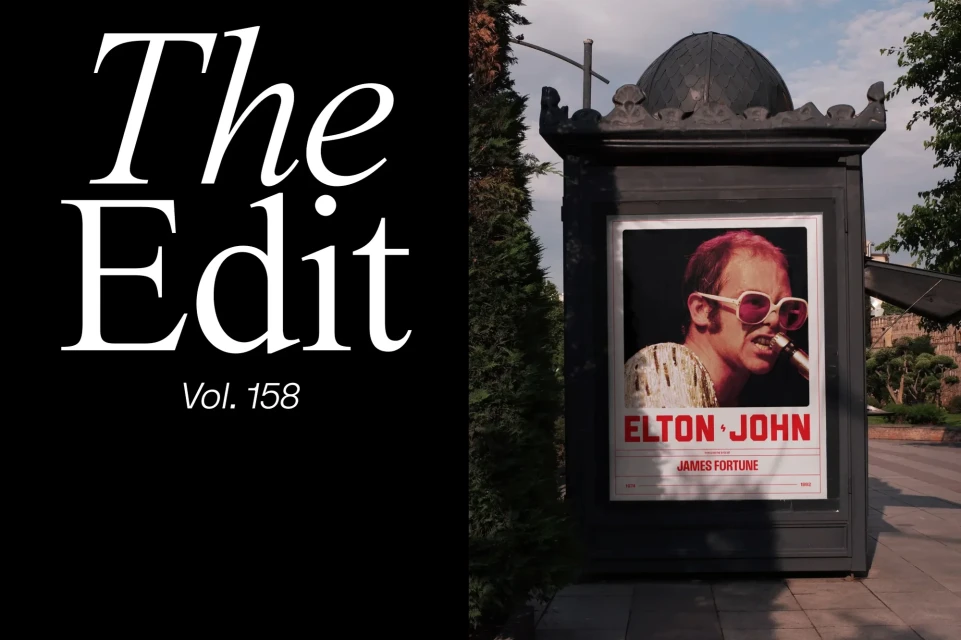 Outdoor magazine stand displays a poster of musician Elton John. The magazine 'The Edit' is written on a black background.
