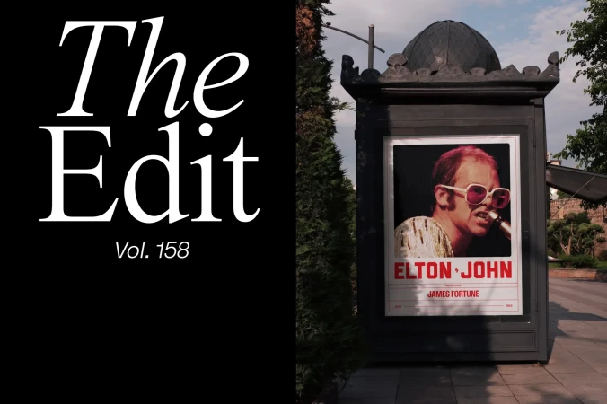 Outdoor magazine stand displays a poster of musician Elton John. The magazine 'The Edit' is written on a black background.
