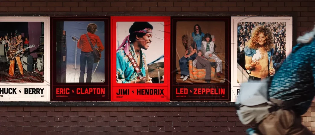 Retro concert posters of Chuck Berry, Eric Clapton, Jimi Hendrix, Led Zeppelin, and Robert Plant on a brick wall outdoors.