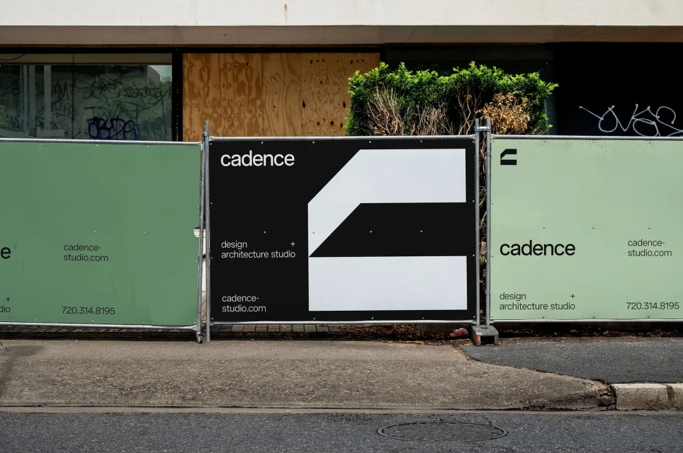 View of outdoor signage with the word cadence and a geometric logo in black and white, in front of a building with covered windows.