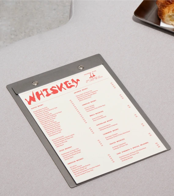 Close-up shot of a stainless steel clipboard displaying a cocktail menu with the word 'Whiskey' in bold red letters.