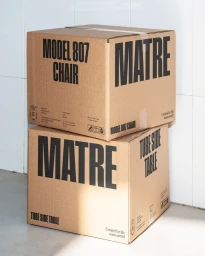 Two stacked brown cardboard shipping boxes with bold black typography reading MATRE and product names against a tiled wall