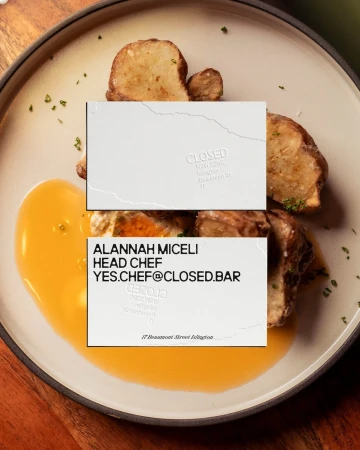 Overhead shot of a tan plate with roasted potatoes, a puddle of orange sauce, and two white business cards.