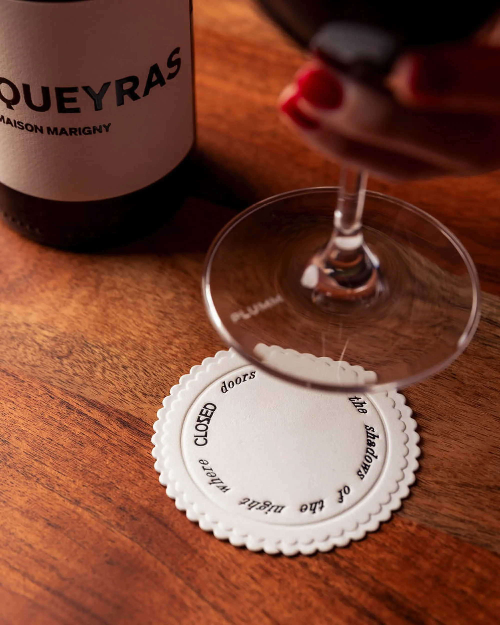 Elevated view of a red wine glass, bottle, and coaster on a wooden surface showcasing a refined beverage still life composition.
