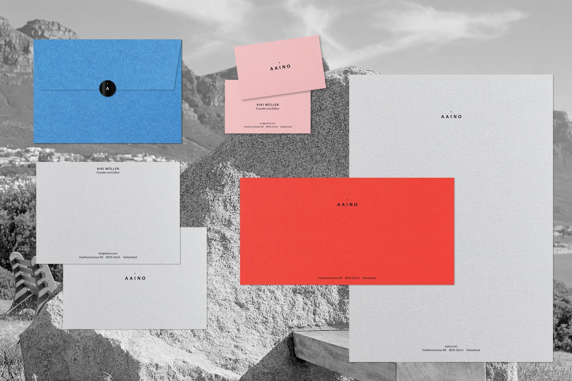 Stationery including a bright blue envelope, a red card, and business cards, sits in front of a monochrome mountain landscape.