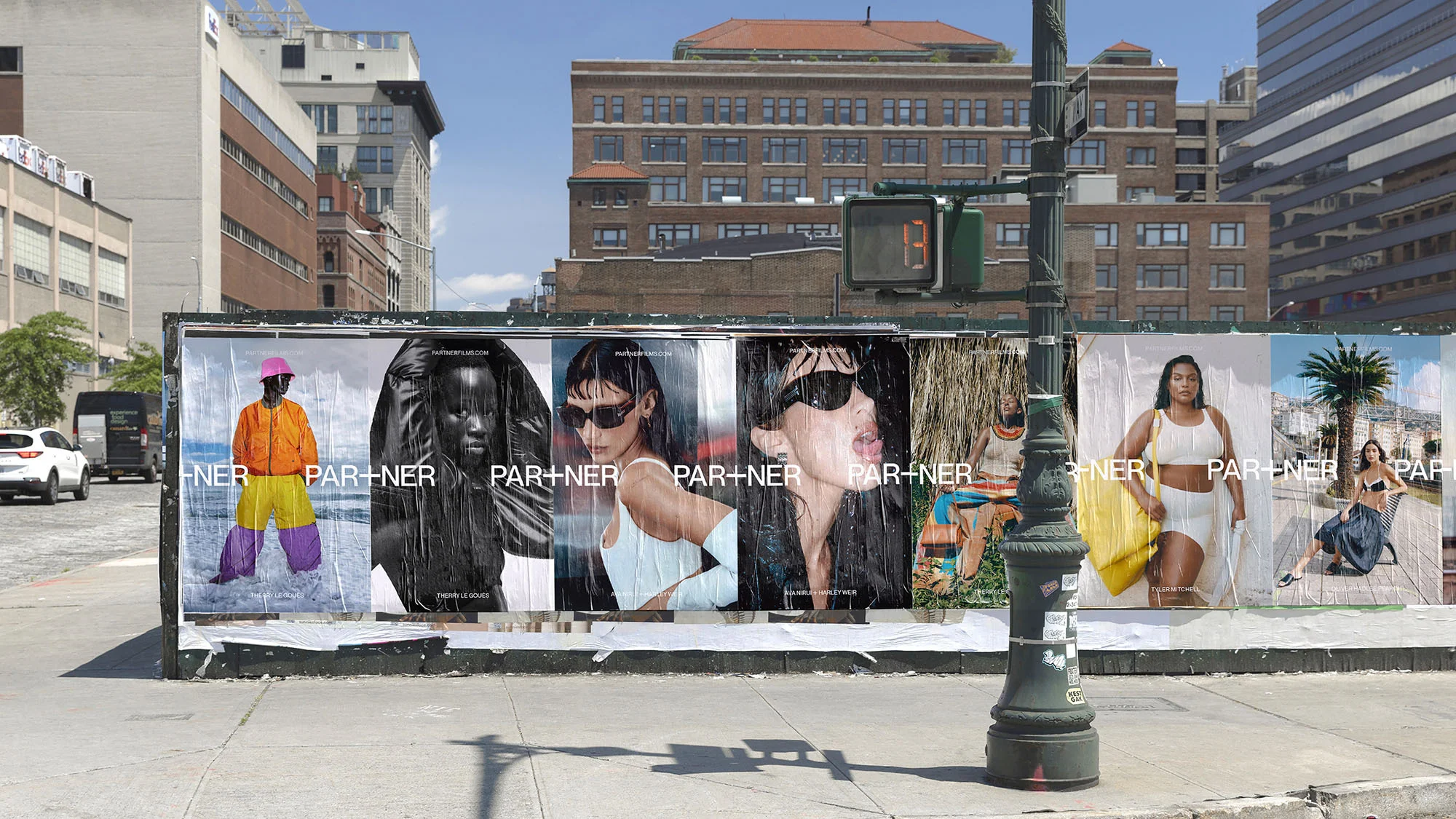 Outdoor view of a bus stop featuring a series of Partner fashion brand posters with diverse models against urban backdrops and bright sunlight.