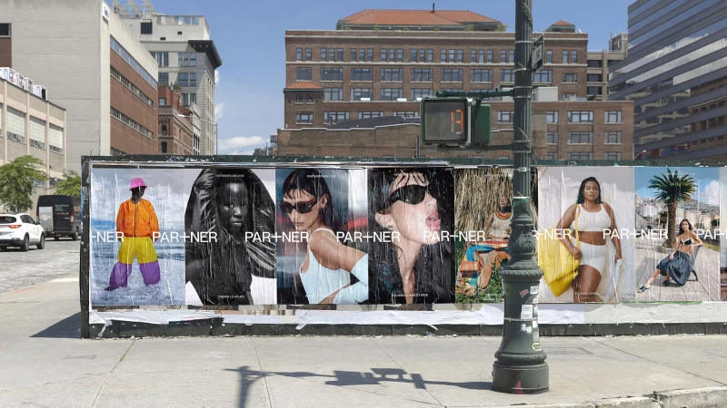 Outdoor view of a bus stop featuring a series of Partner fashion brand posters with diverse models against urban backdrops and bright sunlight.