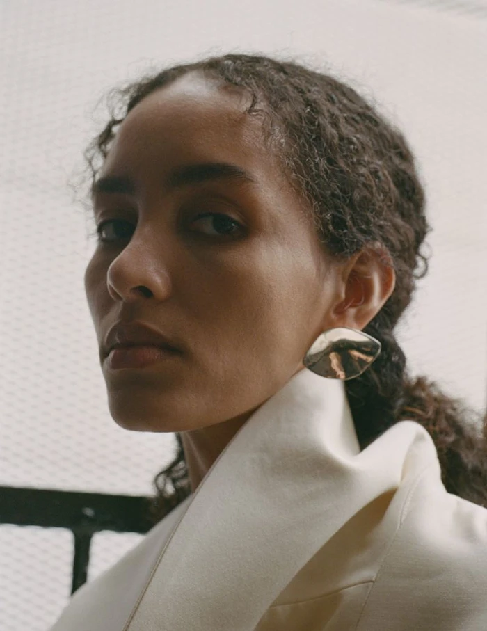 Close-up portrait of a woman wearing an ivory structured coat and an oversized metallic silver earring