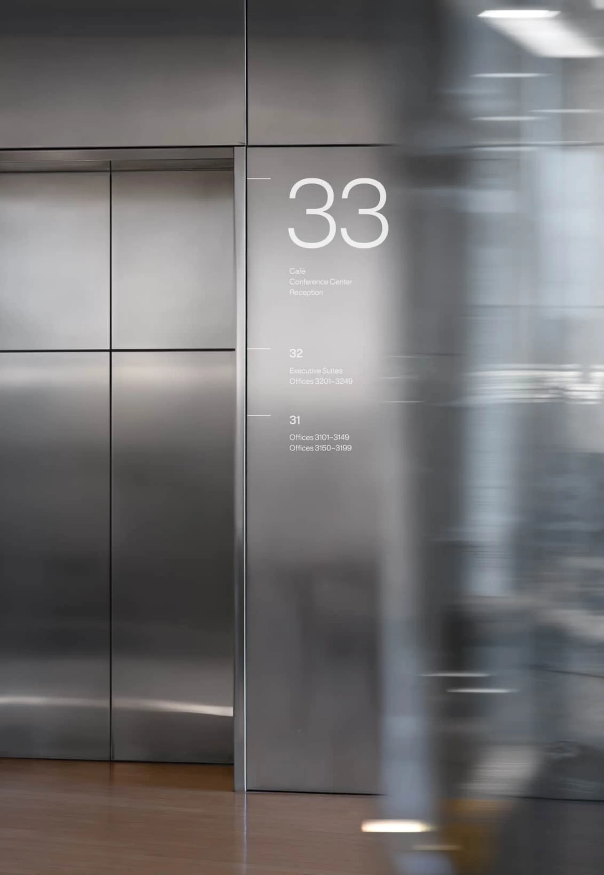 Interior view of a modern building's directory featuring floor numbers and text, next to elevator doors, indicating different levels and offices.