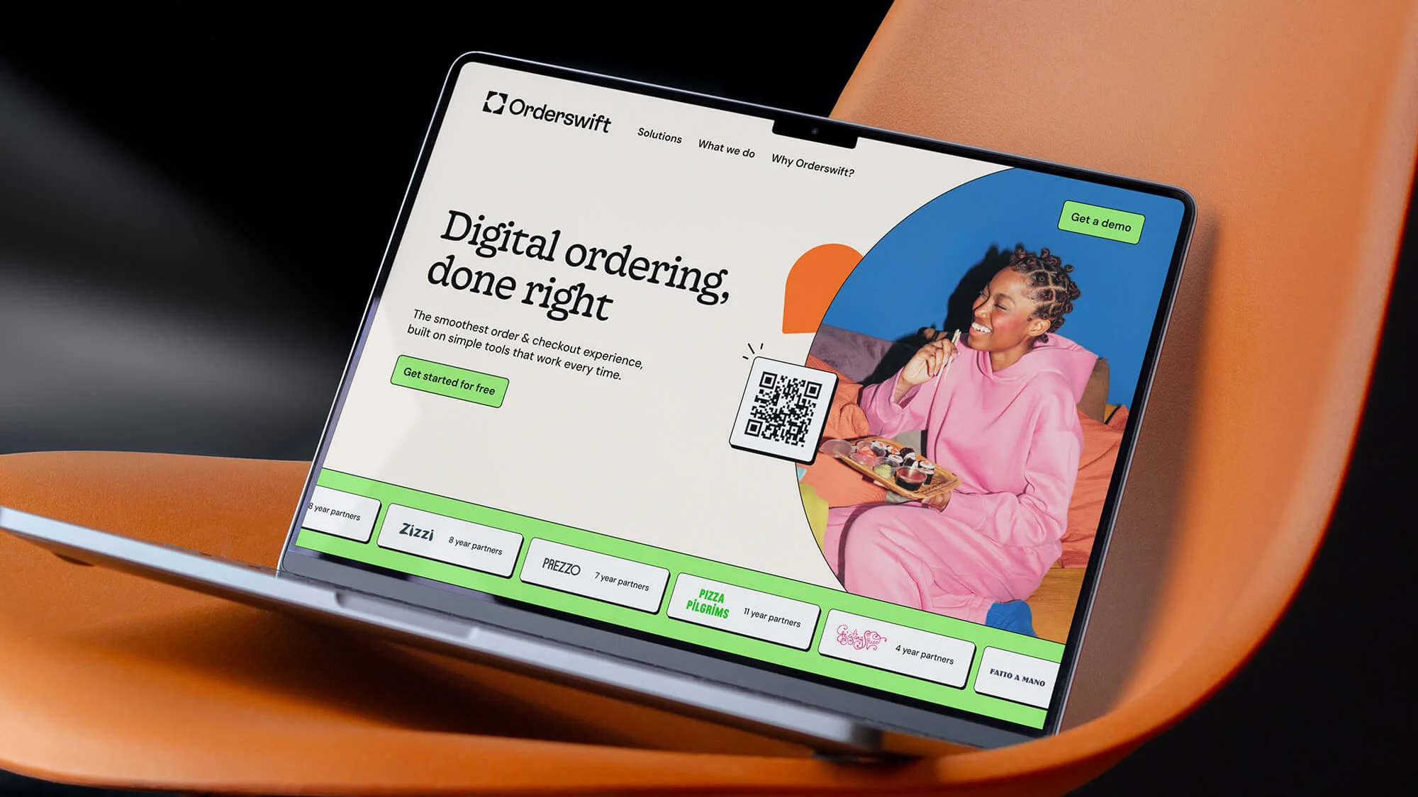 Laptop displaying Orderswift website with woman eating, on an orange chair against dark background, showcasing digital ordering.