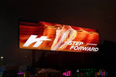 Large outdoor illuminated billboard displaying a Biti's Hunter sneaker with red and orange abstract waves and text step forward.