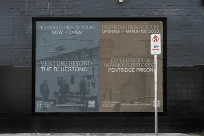 Outdoor poster for Pentridge Prison Tours mounted on a dark grey tiled wall with a parking sign beside it