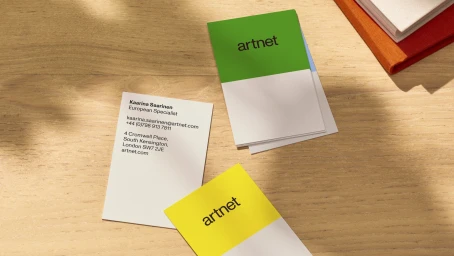 Artnet business cards with green and yellow branding resting on a wooden desk with notebooks.