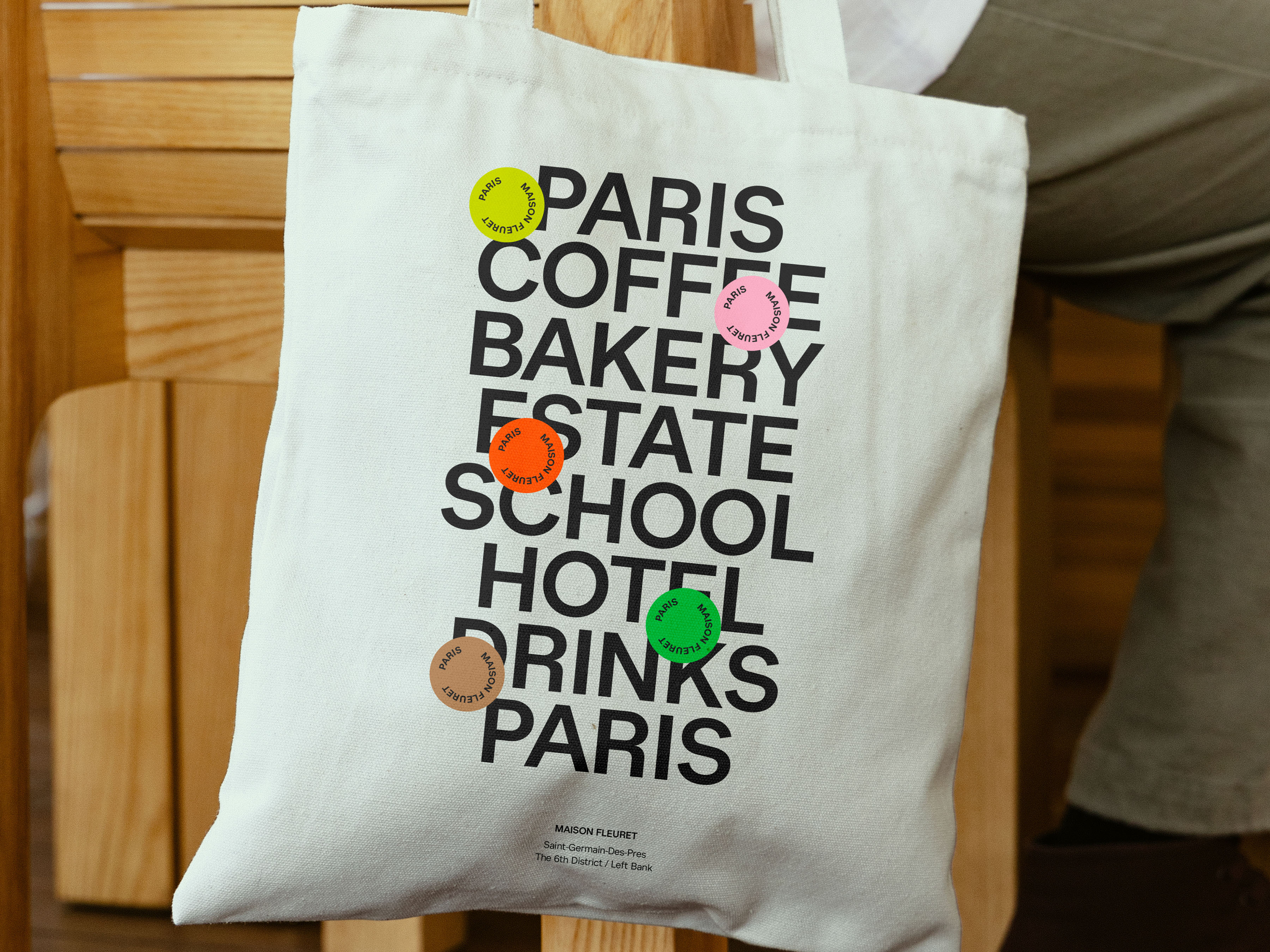 Close-up shot of a white tote bag with black text and colorful circular accents against a wooden background, casual, readable.