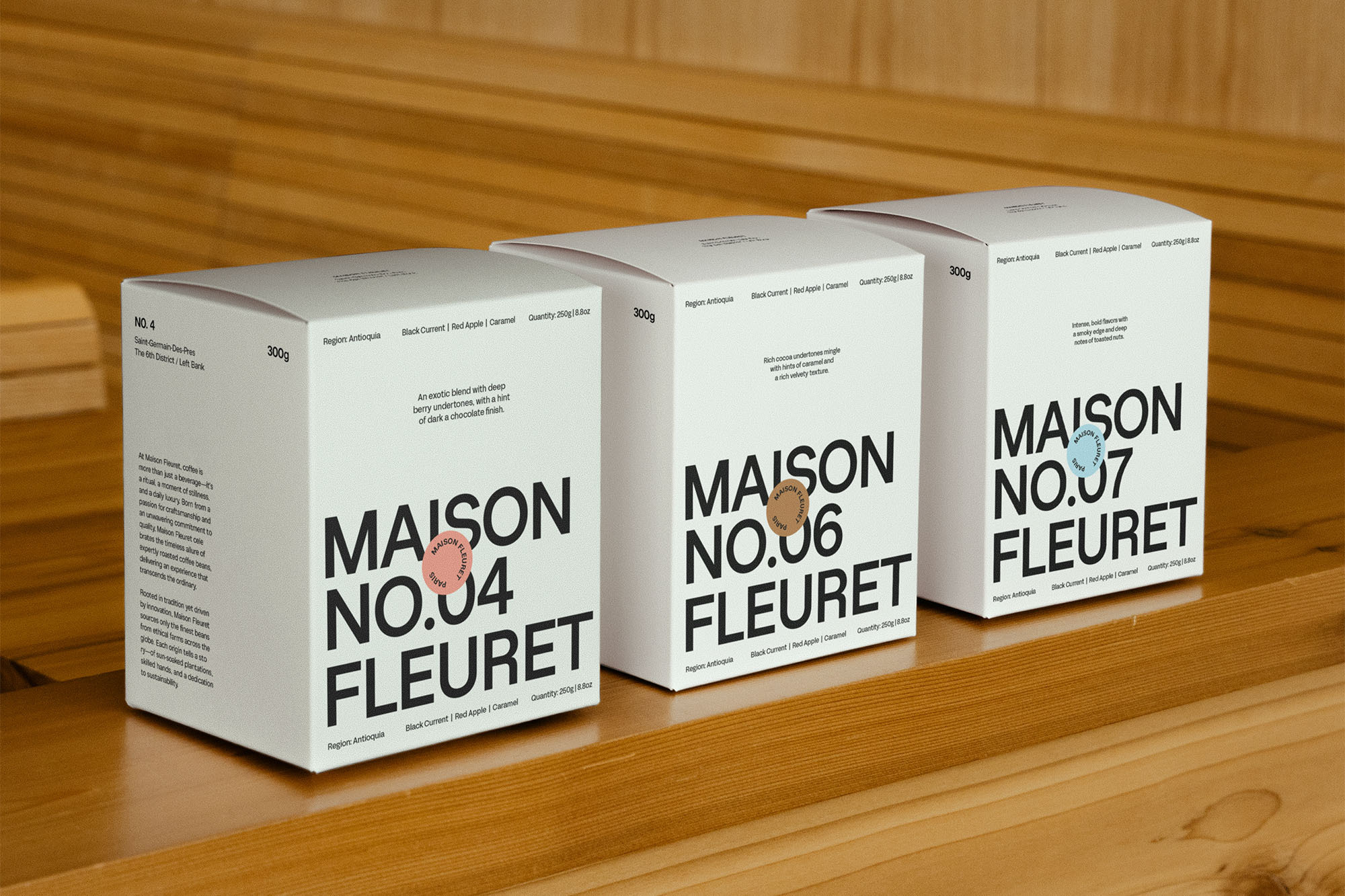 Three white Maison Fleuret chocolate boxes sit on a wooden surface. Each box features black text with a minimalist design.