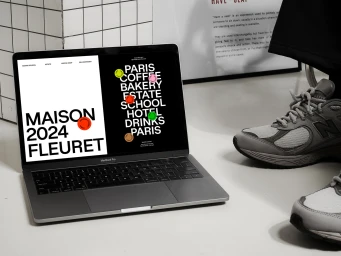 Laptop displaying a brand identity website mockup with typography next to sneakers on a white floor