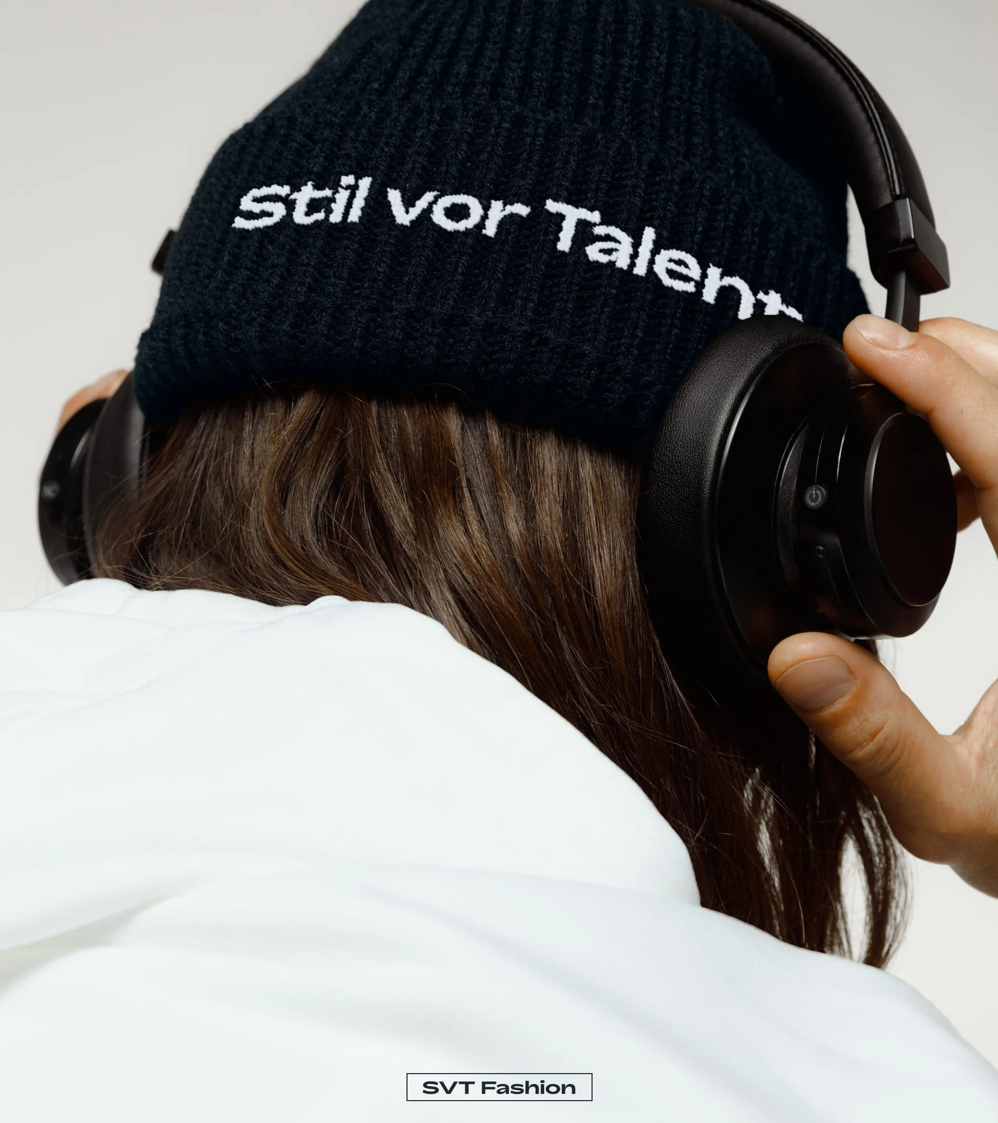Person wearing black 'Stil vor Talent' beanie and headphones against a neutral background in a studio fashion shot.