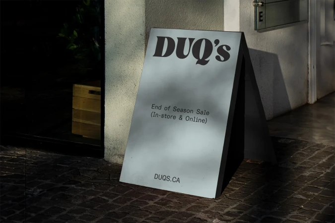 A-frame sign outside a store advertises an end-of-season sale, with the store name 'DUQ's' prominently displayed, creating an eye-catching promotion.