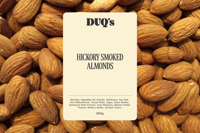Close-up of hickory smoked almonds surrounding a label with text. Food photography showcasing nut snack with focus on branding.
