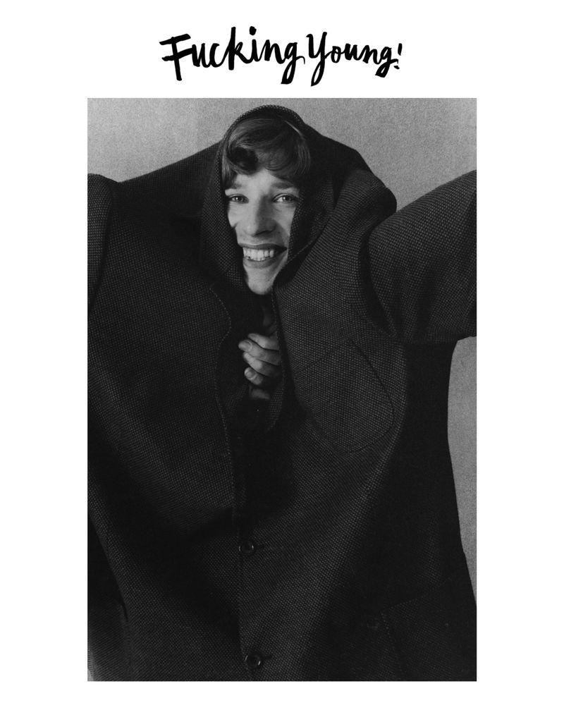 A young adult is joyfully engulfed by a large, dark, textured coat, set against a simple grey backdrop, with 'Fucking Young!' text above.