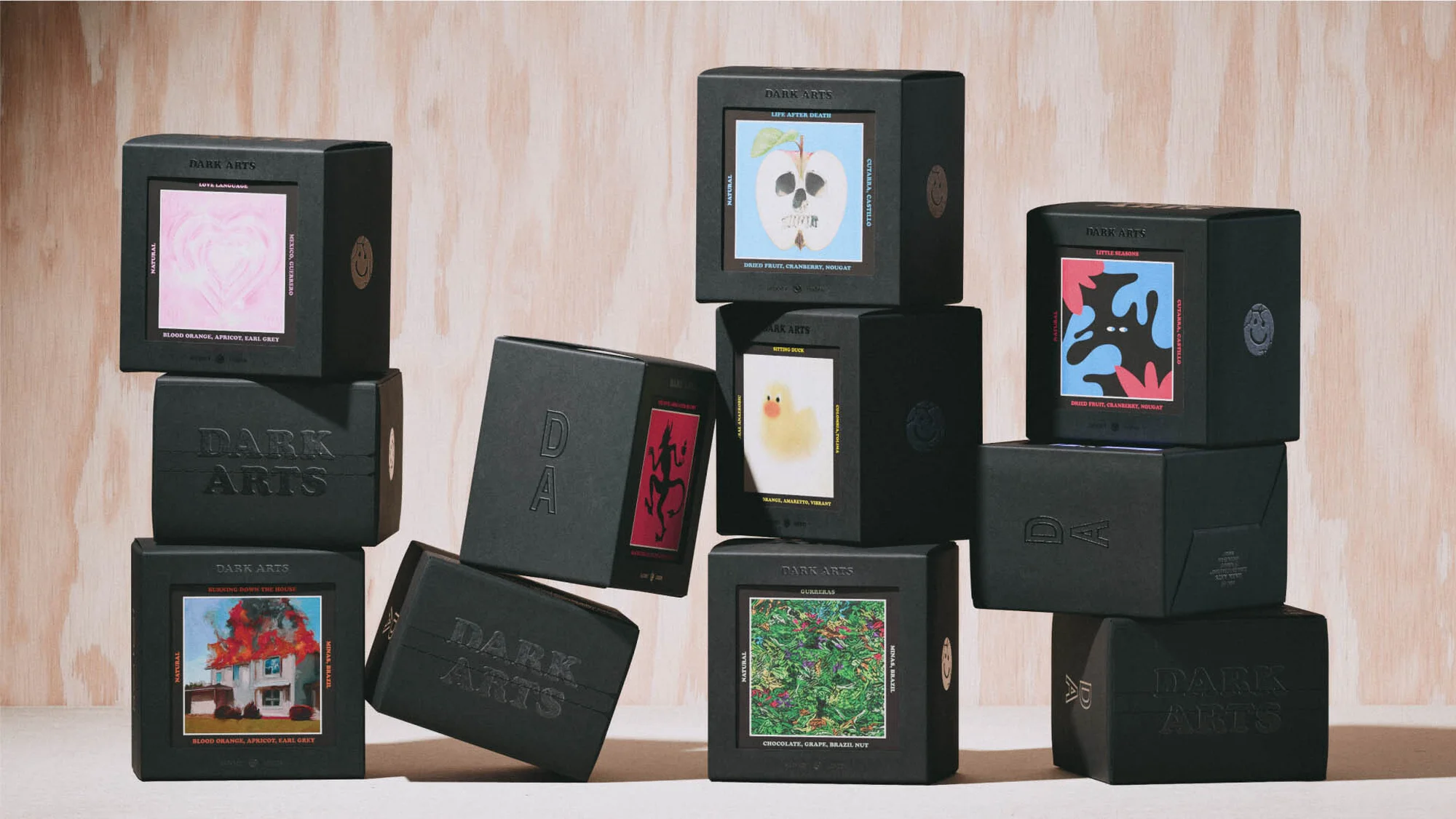 Several black boxes with graphic art on each, stacked and arranged on a light-colored wooden surface in a studio setting.