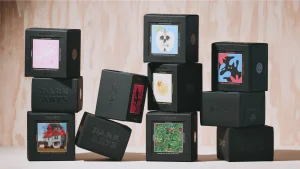 Stacked black coffee boxes with colourful illustrated labels displayed against a pale wooden background