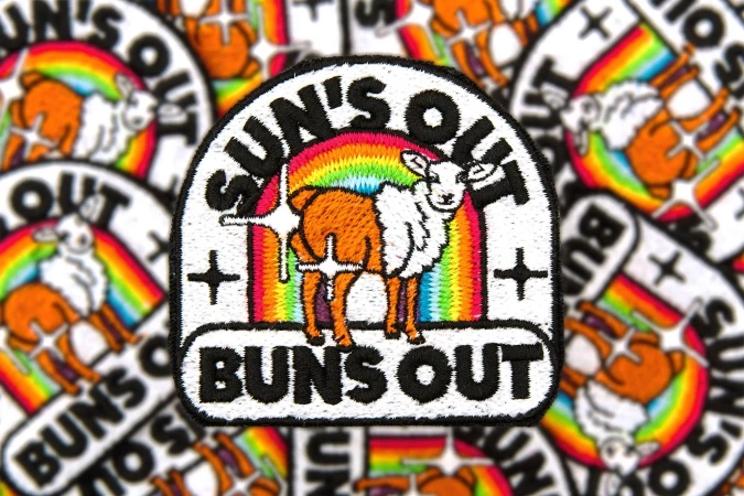 A close-up of multiple embroidered patches featuring a sheep with a rainbow and the text 'Sun's Out Buns Out' on a white background.