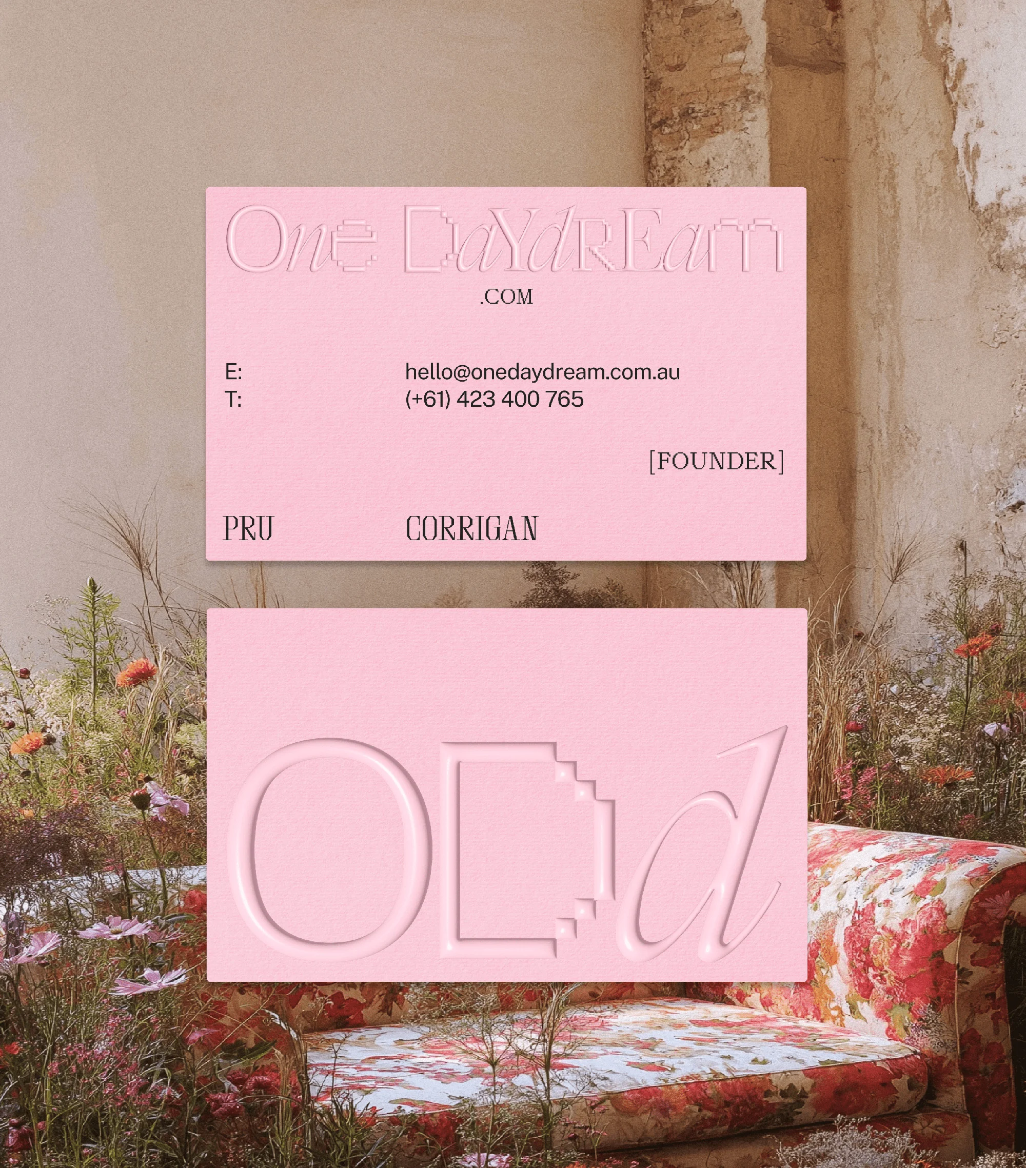 Pink business cards with embossed text and floral setting. Features chair with red floral pattern, surrounded by flowers and natural light.