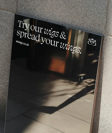 Advertisement featuring a dark background with the text 'Try our wigs & spread your wings' and an image reflecting the outdoors.