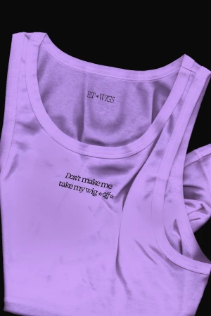 Lilac-colored tank top with a round neck displays 'Don't make me take my wig off' text. Fashion apparel on a dark background.