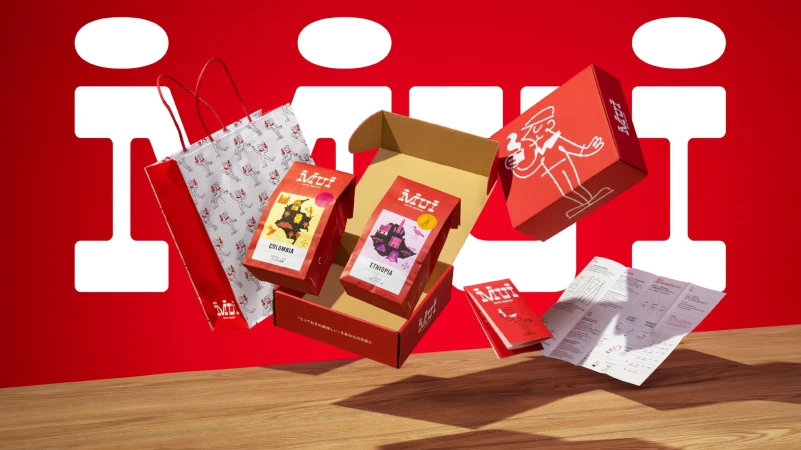 Still life shot of Mui coffee product packaging and promotional material including boxes, bags, and pamphlets against a red backdrop.