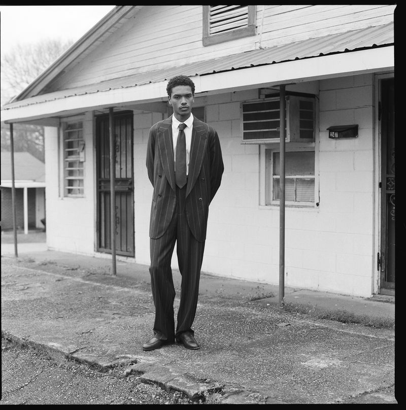 Monochrome portrait of a stylish adult male in a pinstripe suit standing outdoors in front of a building, showcasing fashion and urban style.