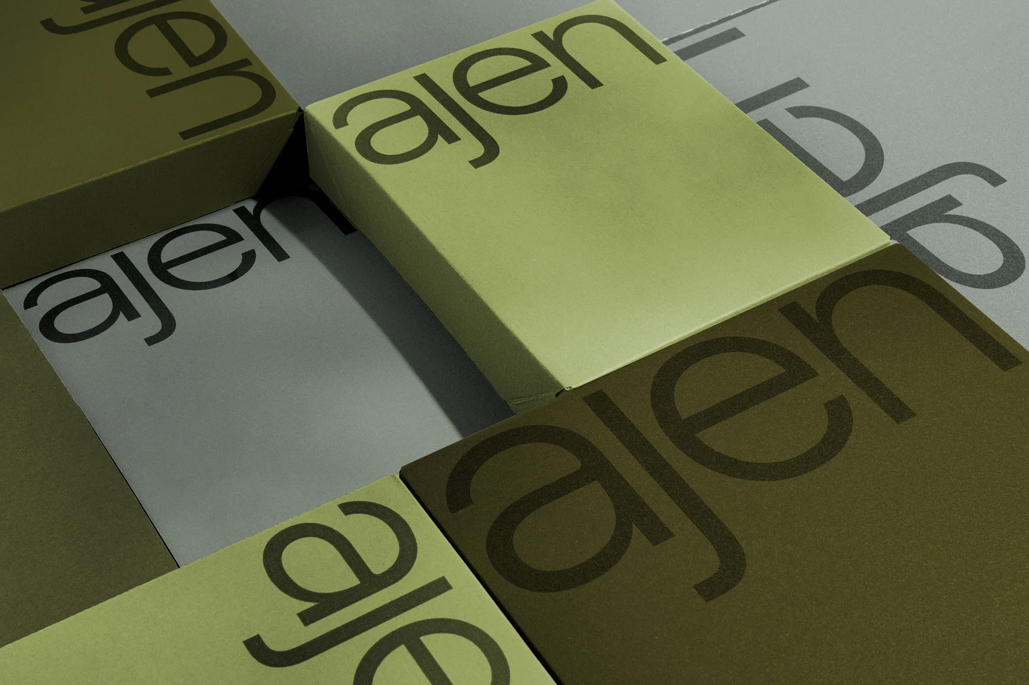 Geometric stack of branded product boxes in olive, khaki, and gray tones with visible 'ajen' text, creating a modern, minimalist pattern.